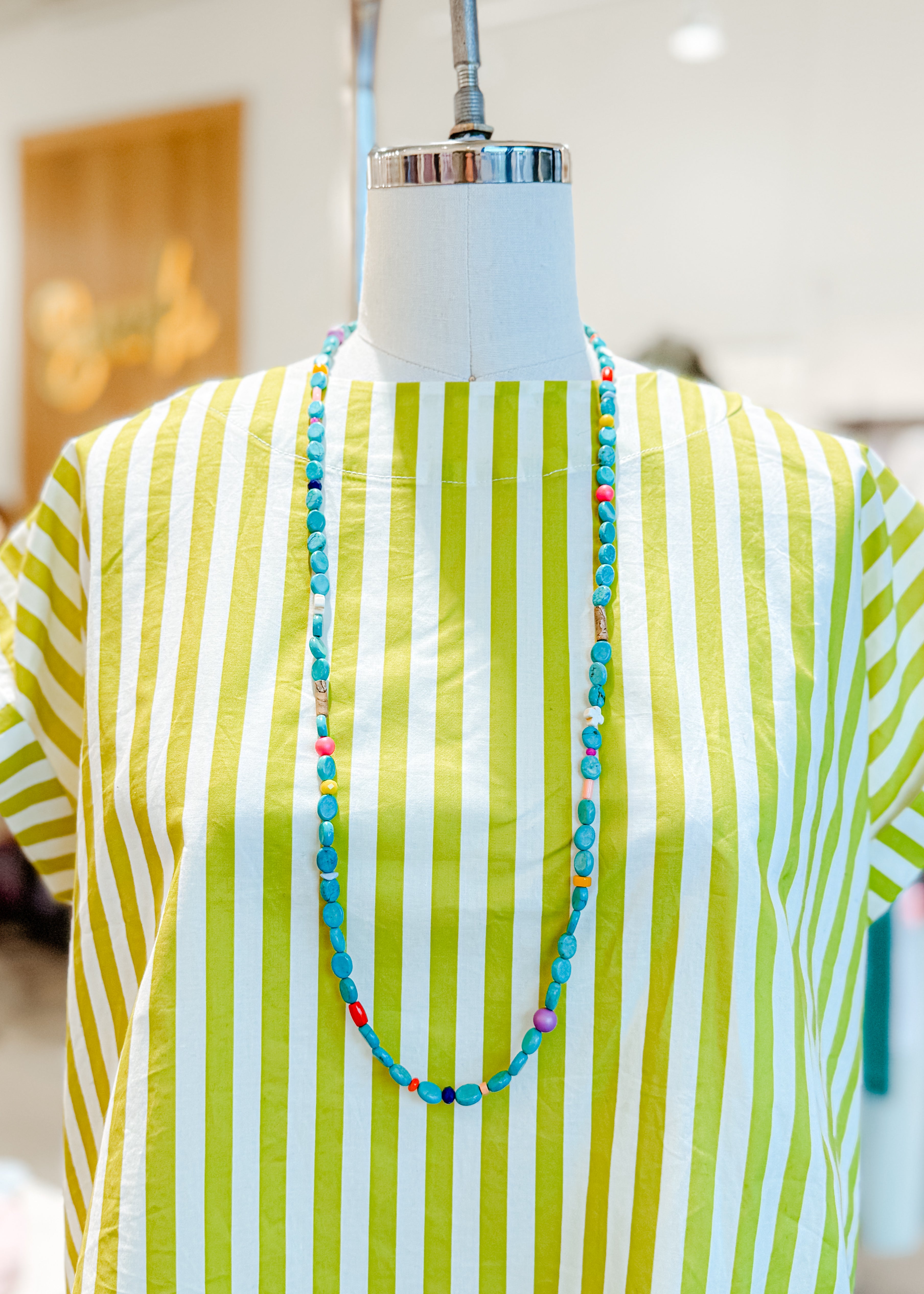 Mannequin wearing a green and white striped shirt with a colorful necklace.