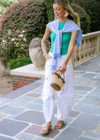 Woman in a green top and white pants with a blue and white checkered scarf, standing on a stone path.