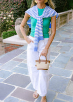 Woman in green top and white pants with a blue and white striped scarf, standing on a stone path.