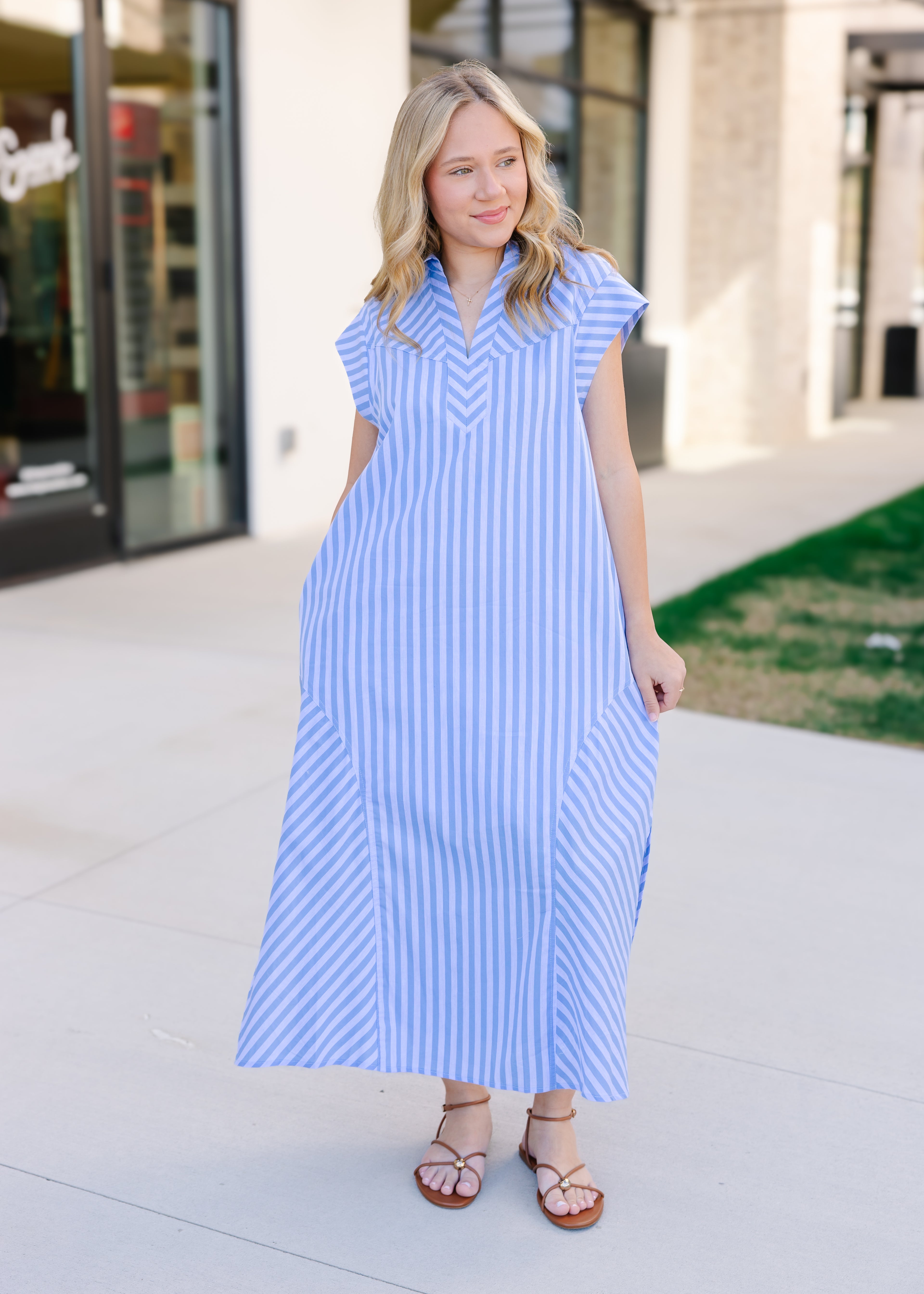 Woman wearing a blue and white striped dress standing on a sidewalk.