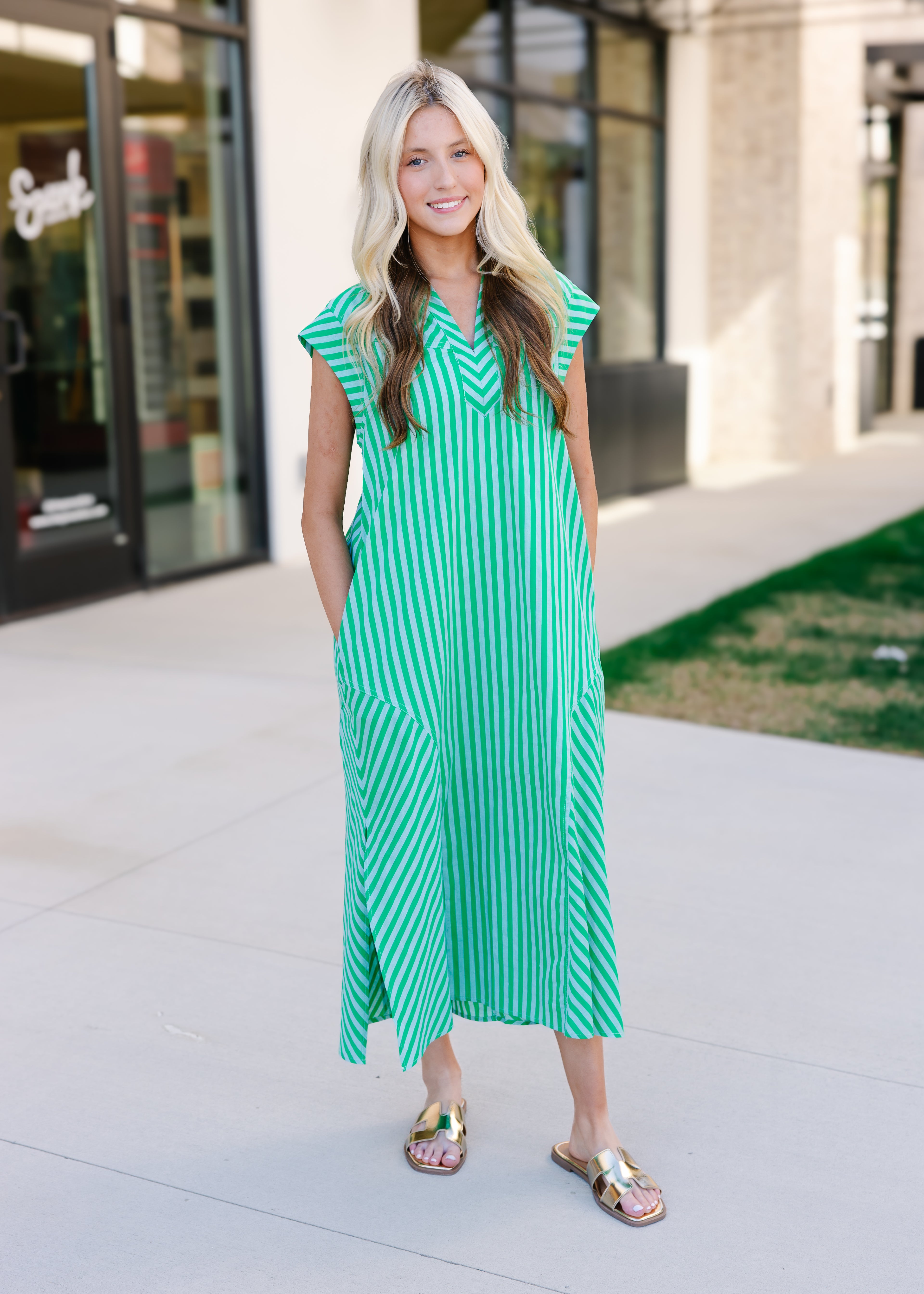 Woman wearing a green and white striped dress standing on a sidewalk.