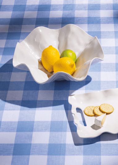 Two white ceramic dishes with lemon slices on a blue and white checkered tablecloth.