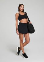 Woman in black athletic wear holding a black bag on a light gray background