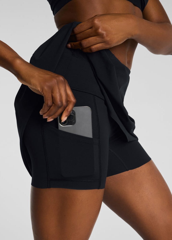 Person wearing black athletic shorts with a pocket on a plain background