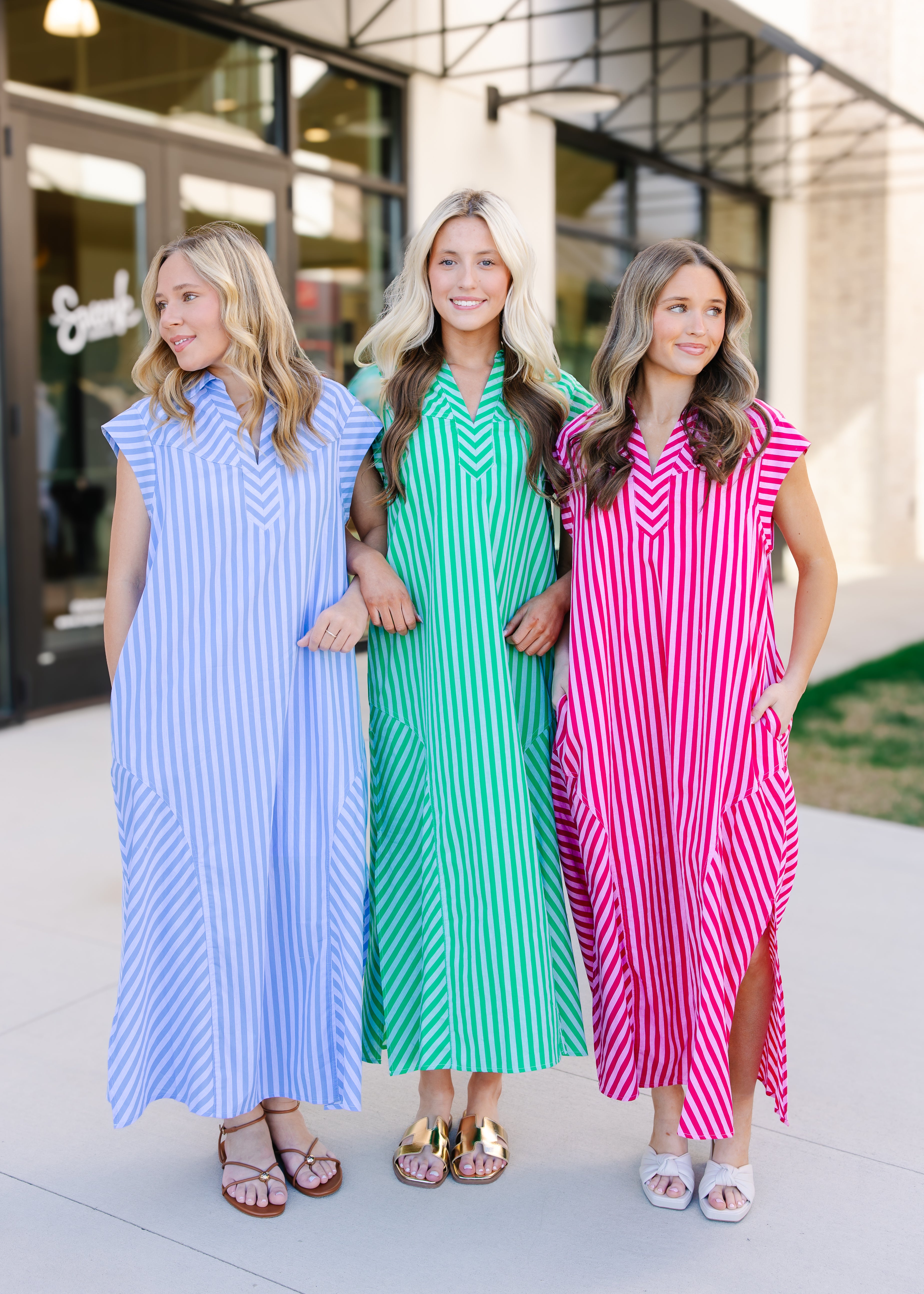 Three women wearing striped dresses standing together outdoors.
