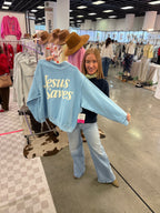 Person holding a blue sweatshirt with 'Jesus Saves' text in a store setting