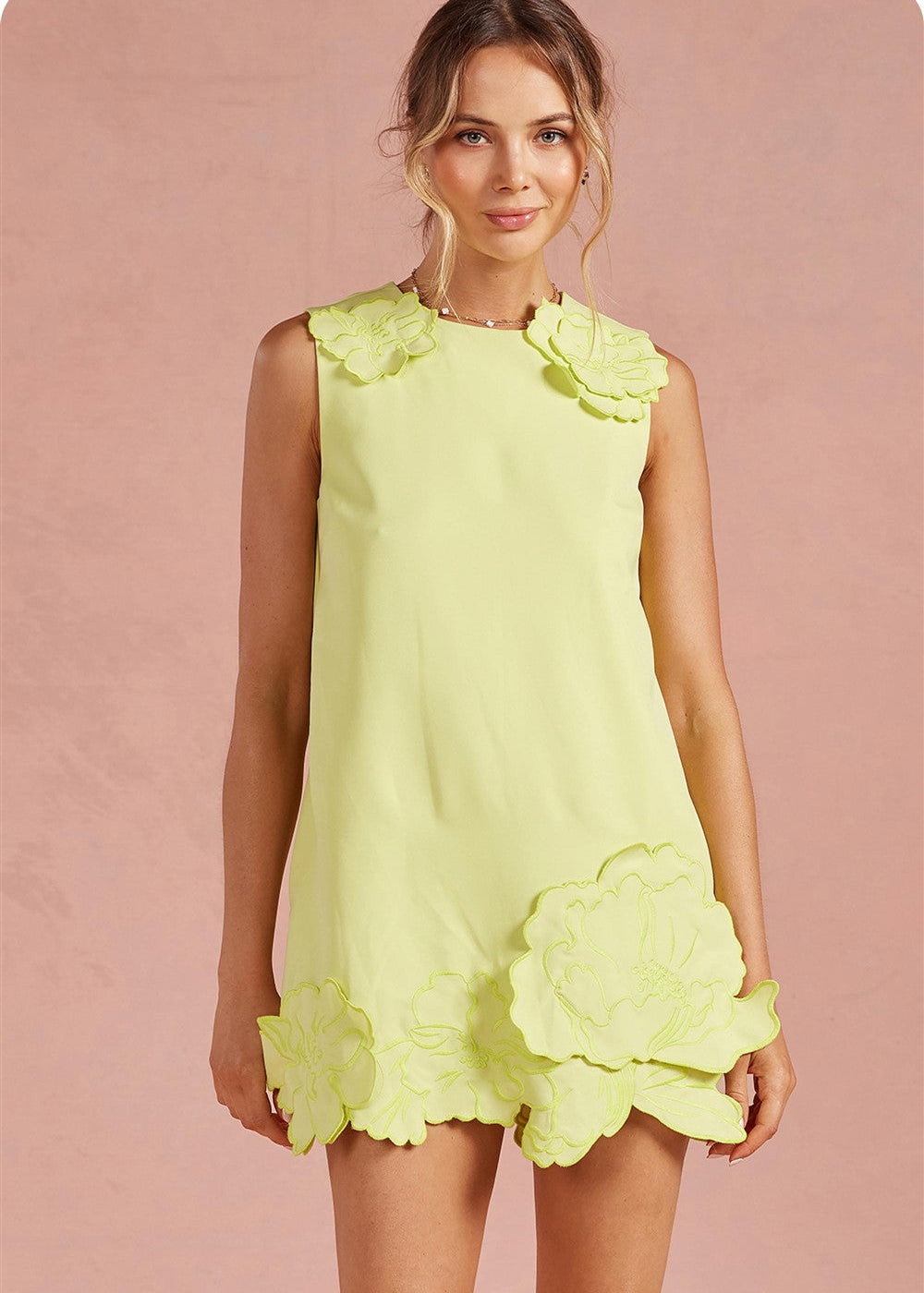 Woman wearing a light green dress with floral details on a pink background