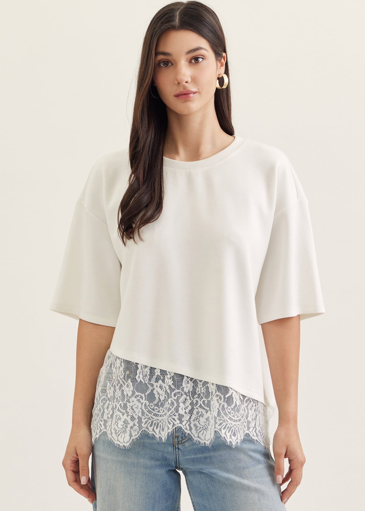 Woman wearing a white blouse with lace trim and blue jeans on a plain background