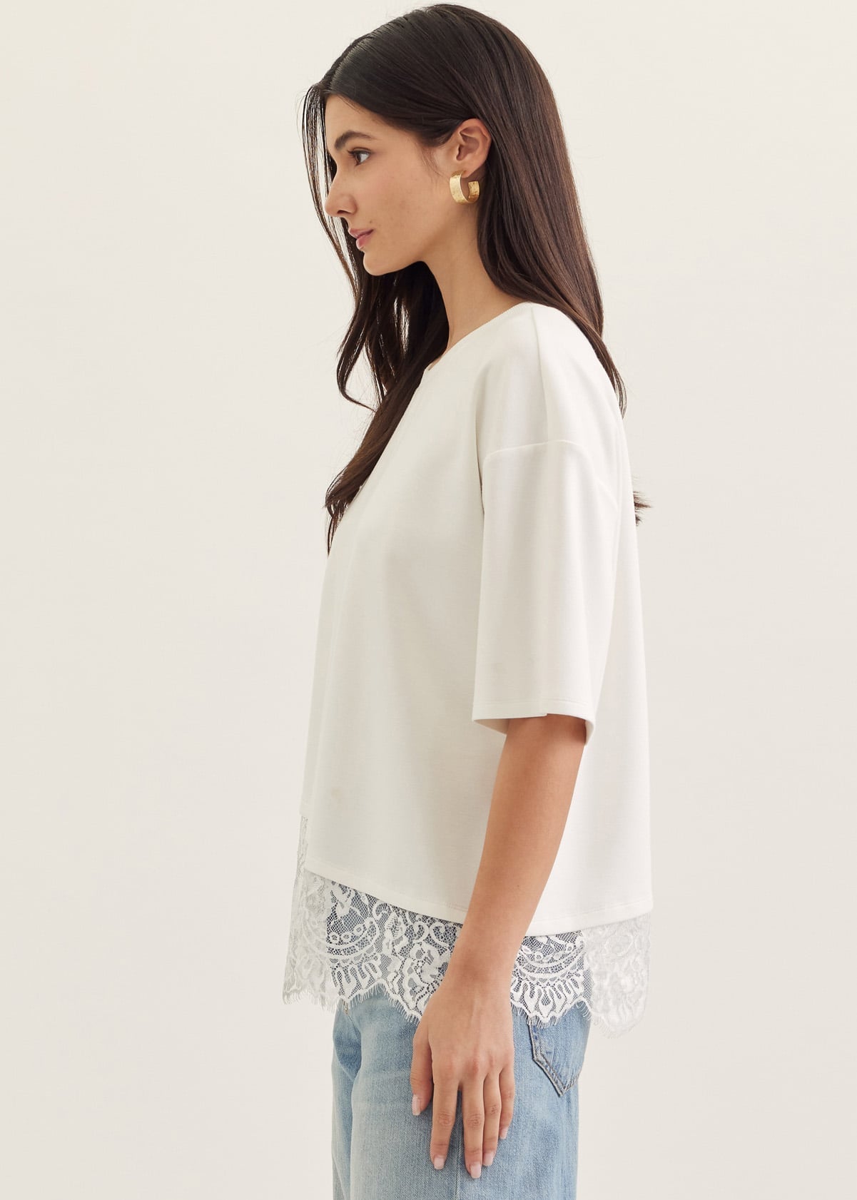 Woman wearing a white blouse with lace trim and light blue jeans on a plain background
