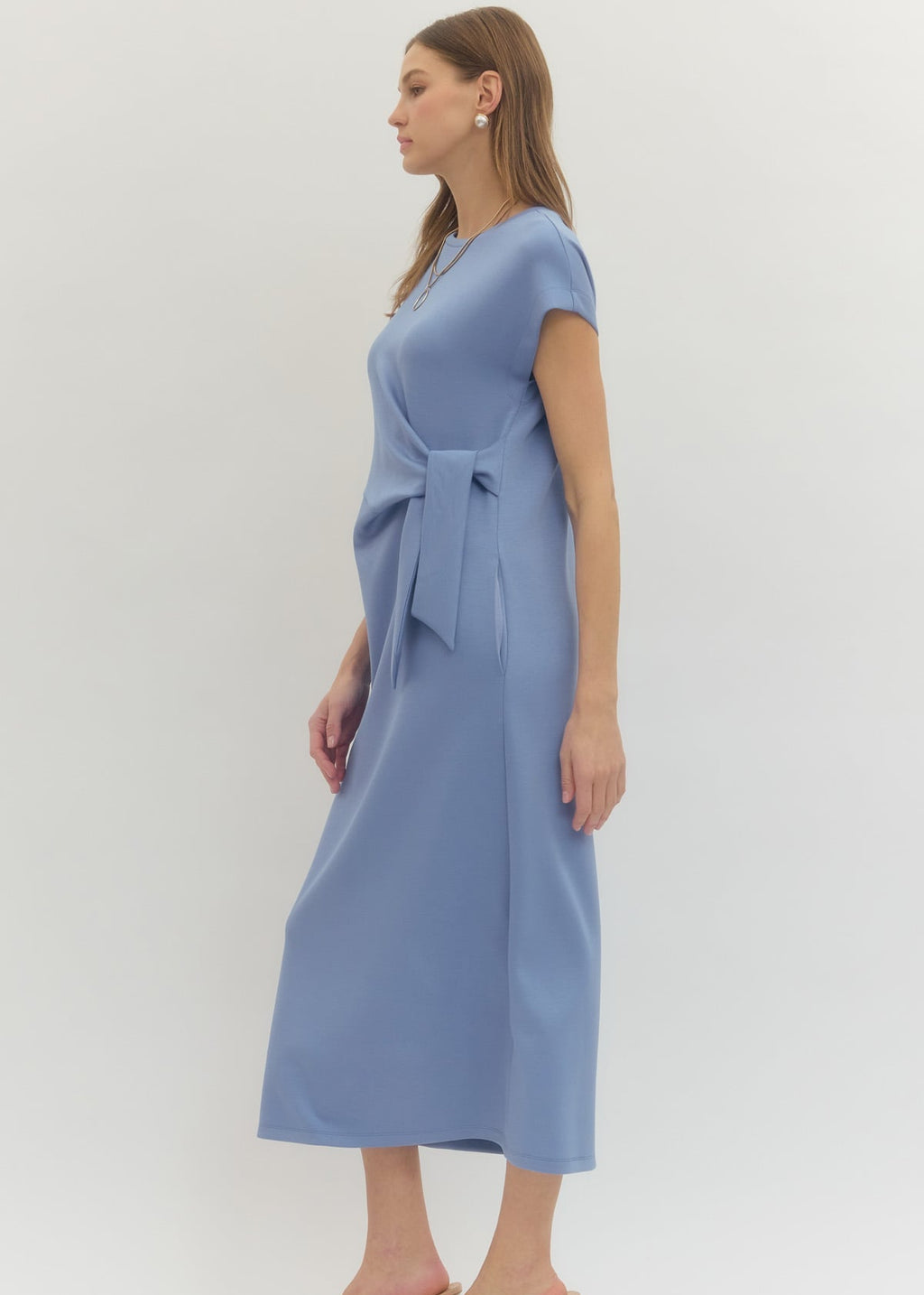 Woman wearing a light blue dress with a tie waist on a white background