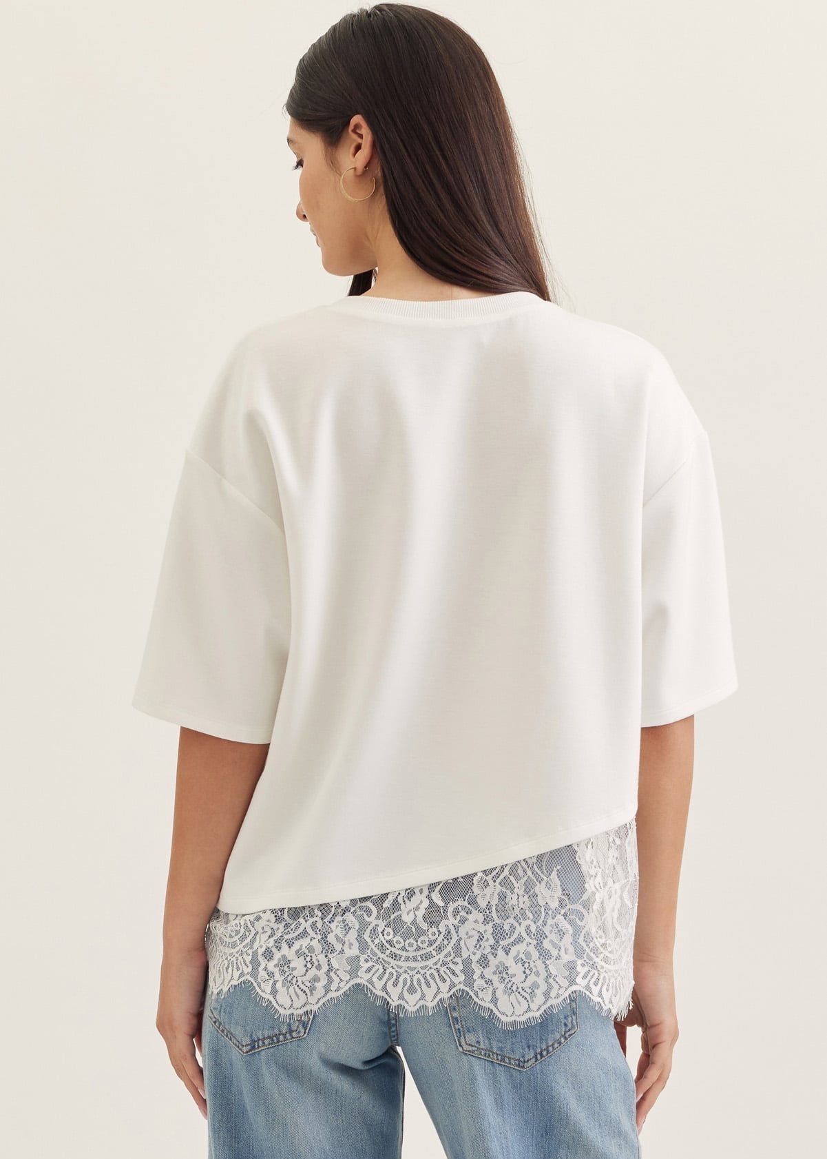 Woman wearing a white blouse with lace trim and blue jeans on a plain background