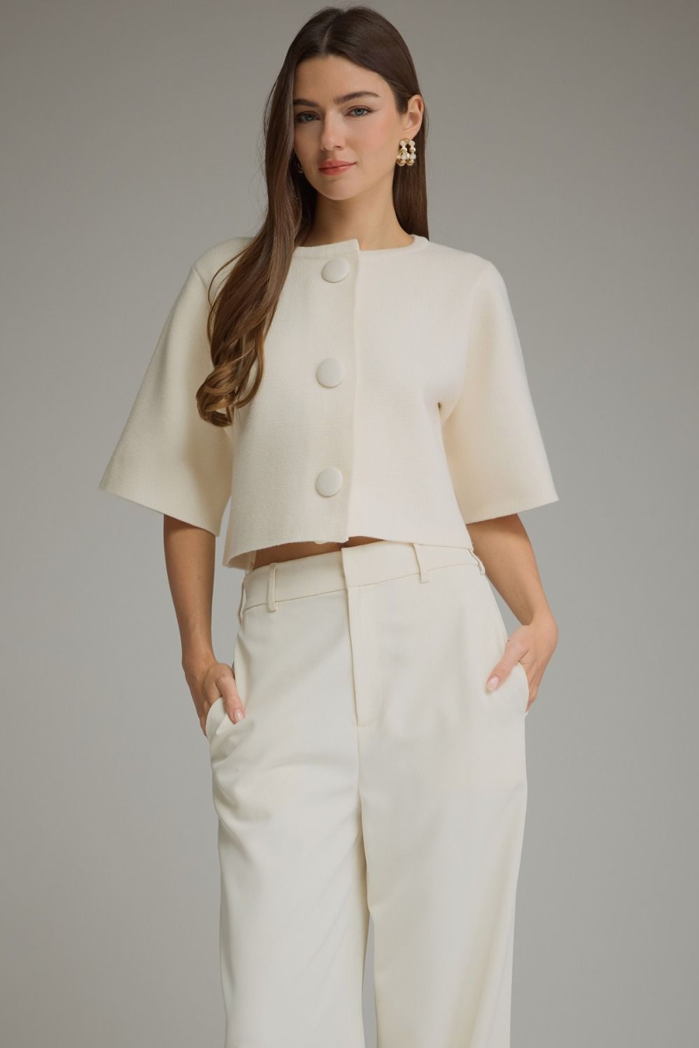 Ivory cropped sweater jacket with short sleeves, round neckline and statement covered buttons, styled with tailored trousers for a classic preppy look.