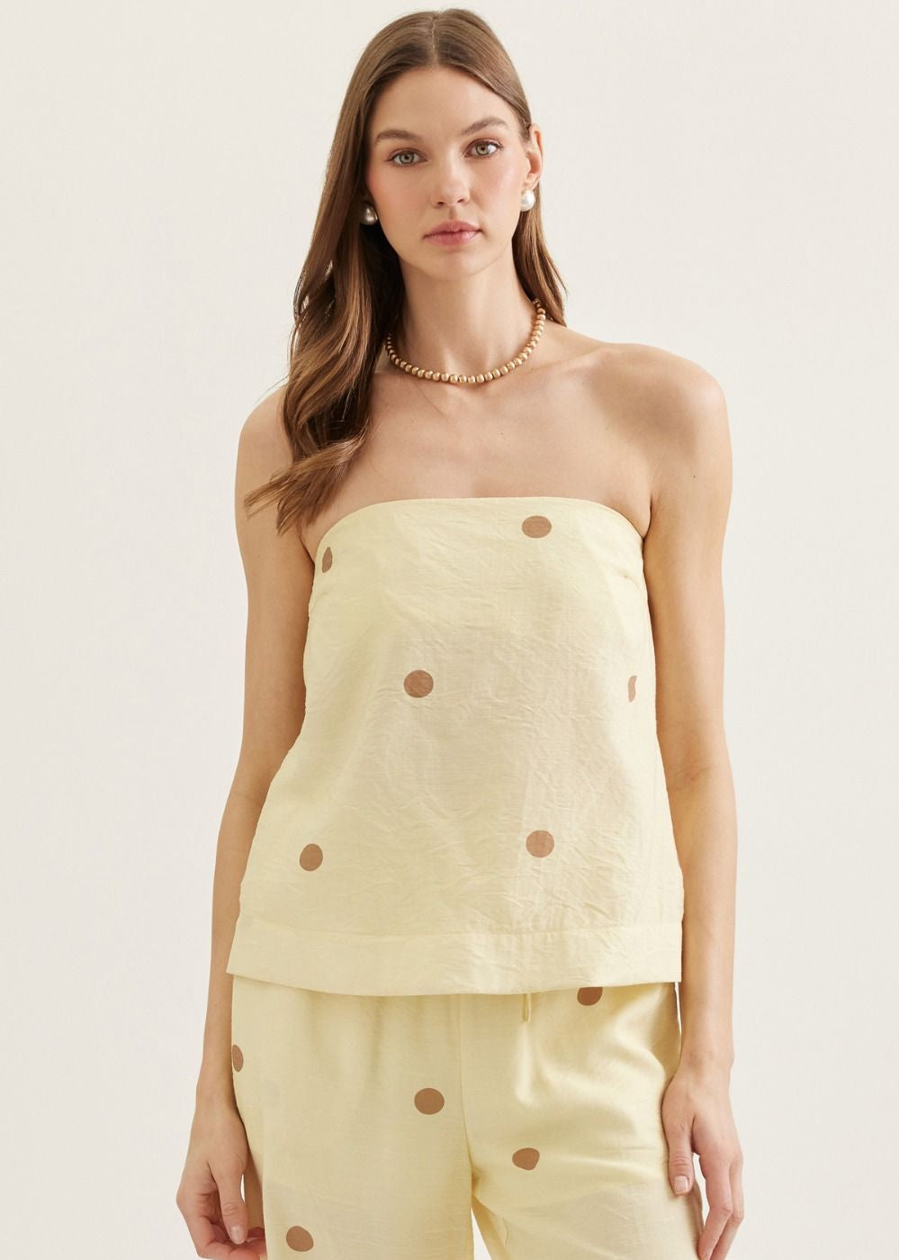 Woman wearing a light yellow strapless top and pants with button details on a plain background