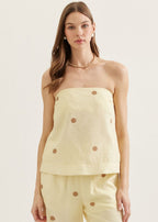 Woman wearing a light yellow strapless top and pants with button details on a plain background