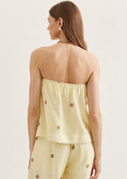 Woman wearing a light yellow strapless top and pants with brown buttons on a beige background