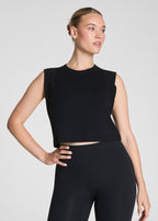 Woman wearing a black sleeveless top and black leggings on a light gray background